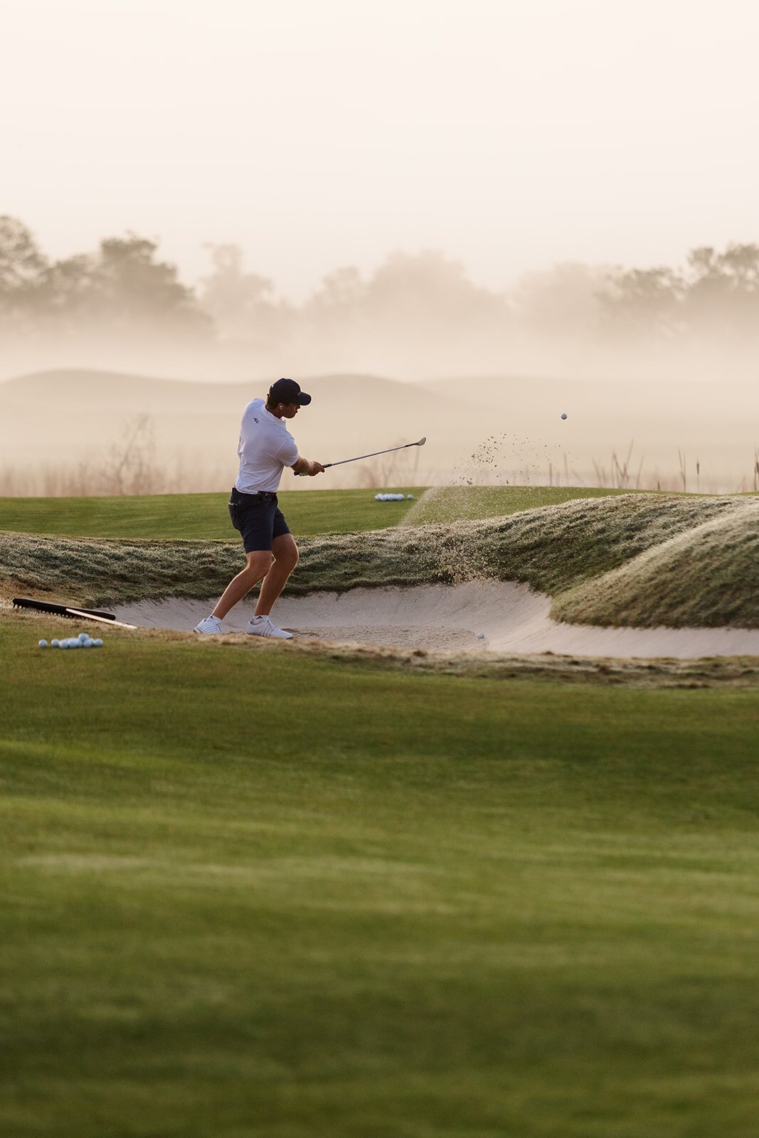 Golfer hitting a bunker shot through morning fog at The Ford